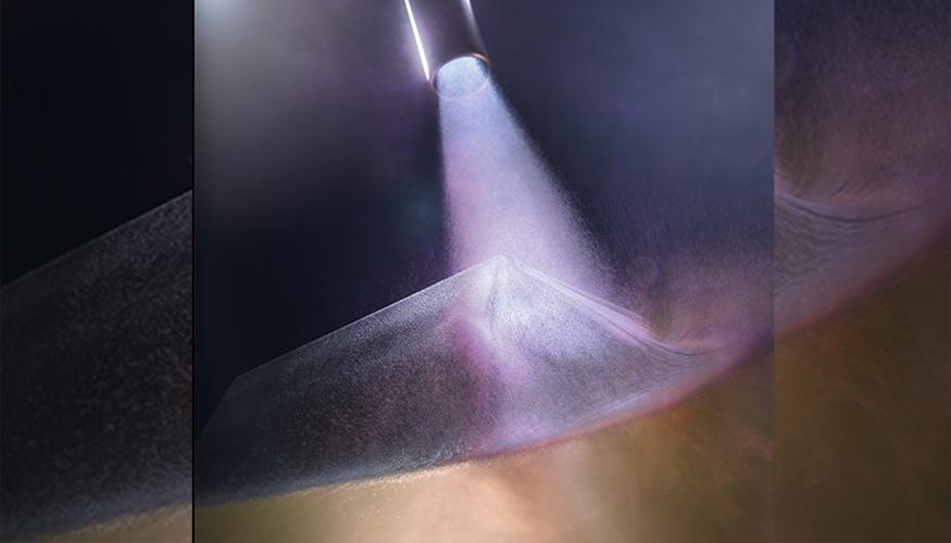 A cold-spray chamber is shown during deposition, with the nozzle at the top of the image and a near-full density sample being fabricated in the center. Particles of the brittle thermoelectric bismuth telluride are accelerated to more than 900 meters per second, or almost Mach 3, in inert gas and directed onto a copper surface, laying down the strips that form the basis of a functioning thermoelectric generator to harvest waste heat. Graphic by Jacob Long/LLNL