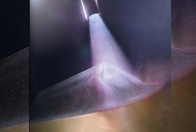 A cold-spray chamber is shown during deposition, with the nozzle at the top of the image and a near-full density sample being fabricated in the center. Particles of the brittle thermoelectric bismuth telluride are accelerated to more than 900 meters per second, or almost Mach 3, in inert gas and directed onto a copper surface, laying down the strips that form the basis of a functioning thermoelectric generator to harvest waste heat. Graphic by Jacob Long/LLNL