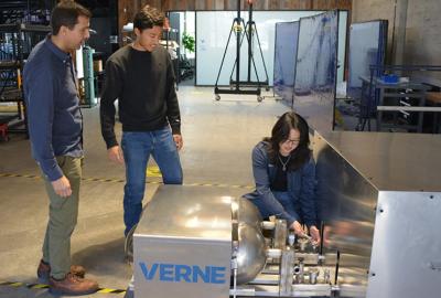 From left to right, Nick Killingsworth, a mechanical engineer at LLNL, and Telis Athanasopoulos Yogo, a Verne mechanical engineer, watch as Kara Zhang, a Verne process engineer, installs a vacuum pressure gauge on the system.